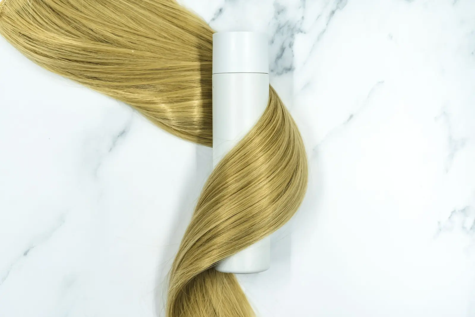 White haircare bottle next to a twist of blonde hair on marble