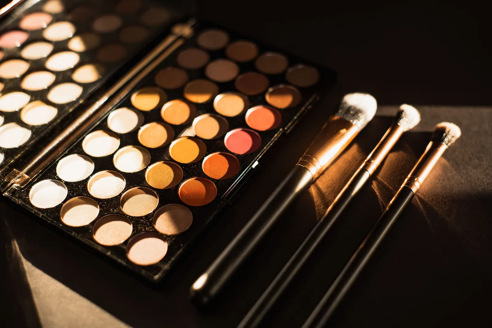 Eyeshadow palette with warm shimmer shades and makeup brushes on a dark surface