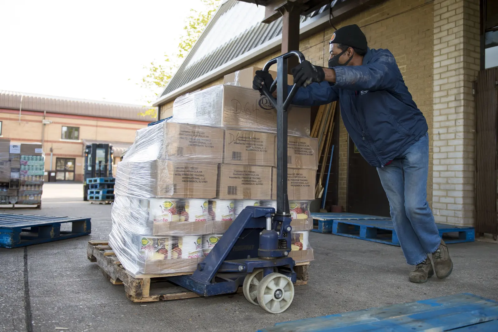 Warehouse worker moving a pallet of boxed goods with a pallet jack