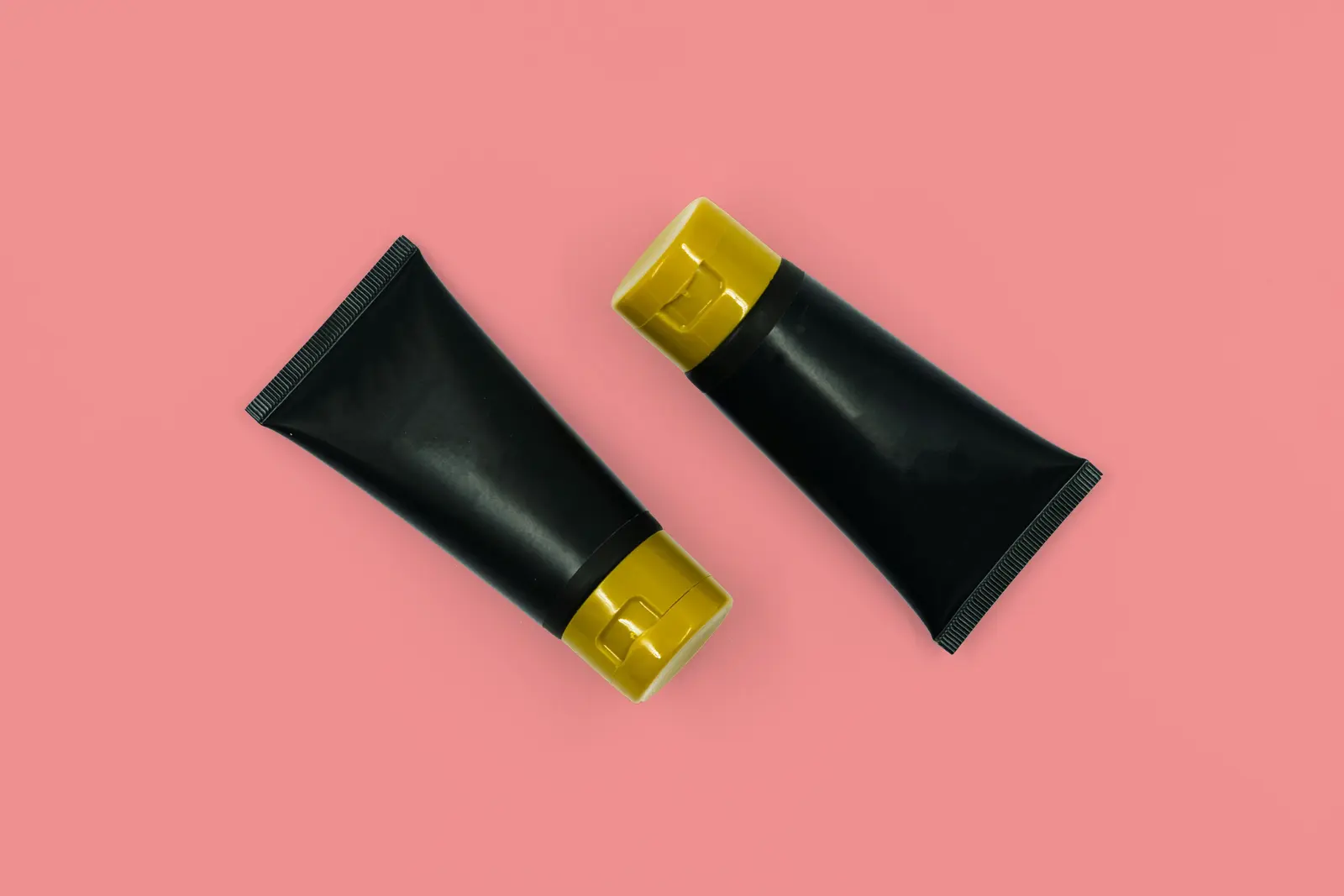 Two black cosmetic tubes with gold caps on a pink background